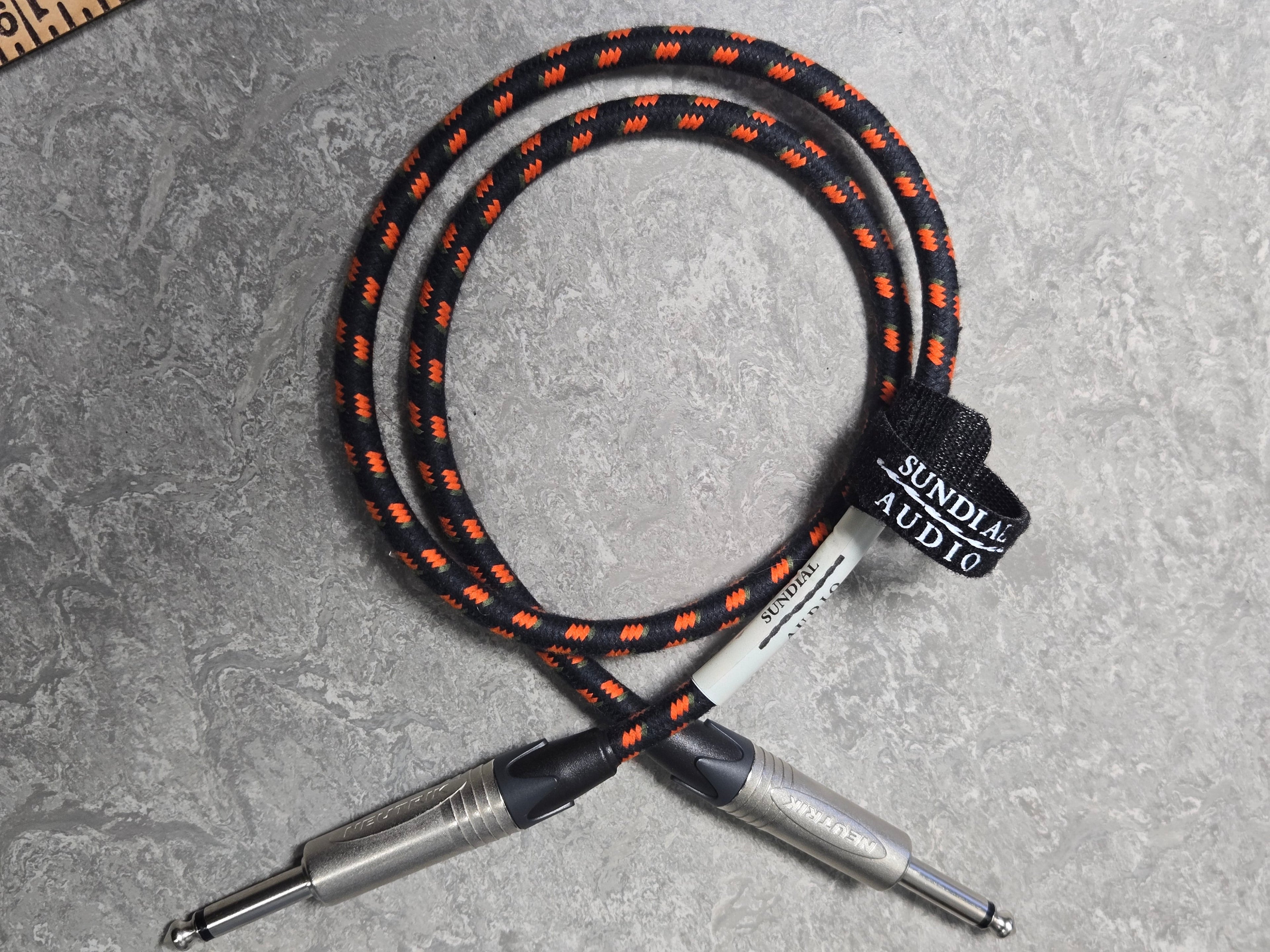 Black and orange braided audio cable with silver connectors on a gray surface